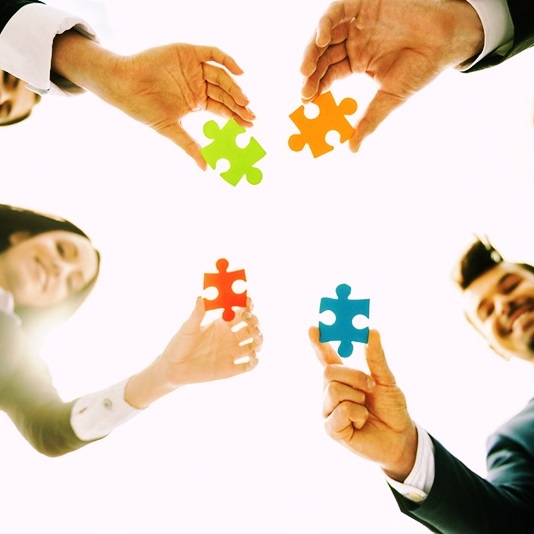 Closeup of business people wanting to put four pieces of puzzle together. Team work.